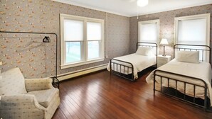 A bedroom with two single beds, a chair, a standing lamp, and a ceiling fan.
