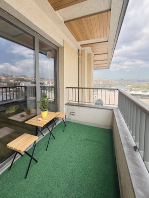 A balcony with a green artificial turf floor, a wooden table, and a potted plant. - 10 Mins to Takism - Central & New Modern Flat (Istanbul)