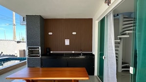 Eine moderne Küche mit Holztisch und Bänken, einer Glastür zum Balkon und einem Pool im Hintergrund.