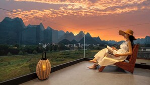 Una mujer sentada en un banco de madera con vistas a montañas y al atardecer.