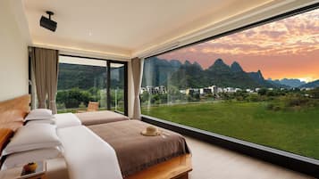 Een slaapkamer met een groot raam, een bed en uitzicht op een bergachtig landschap.