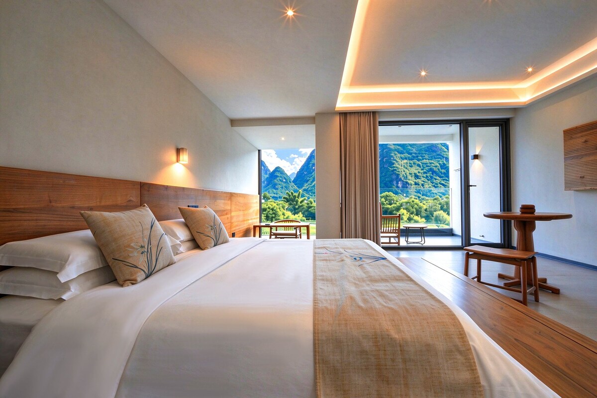 A hotel room with a large bed, a wooden headboard, a view of mountains, and a balcony with a table.