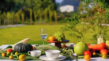 A table set with various fruits, vegetables, and a glass of water, with a scenic outdoor background.