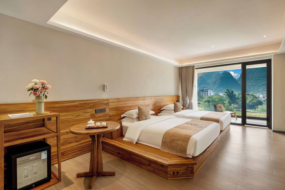 Una habitación de hotel con una cama de madera, una mesita, un refrigerador y vistas a las montañas.