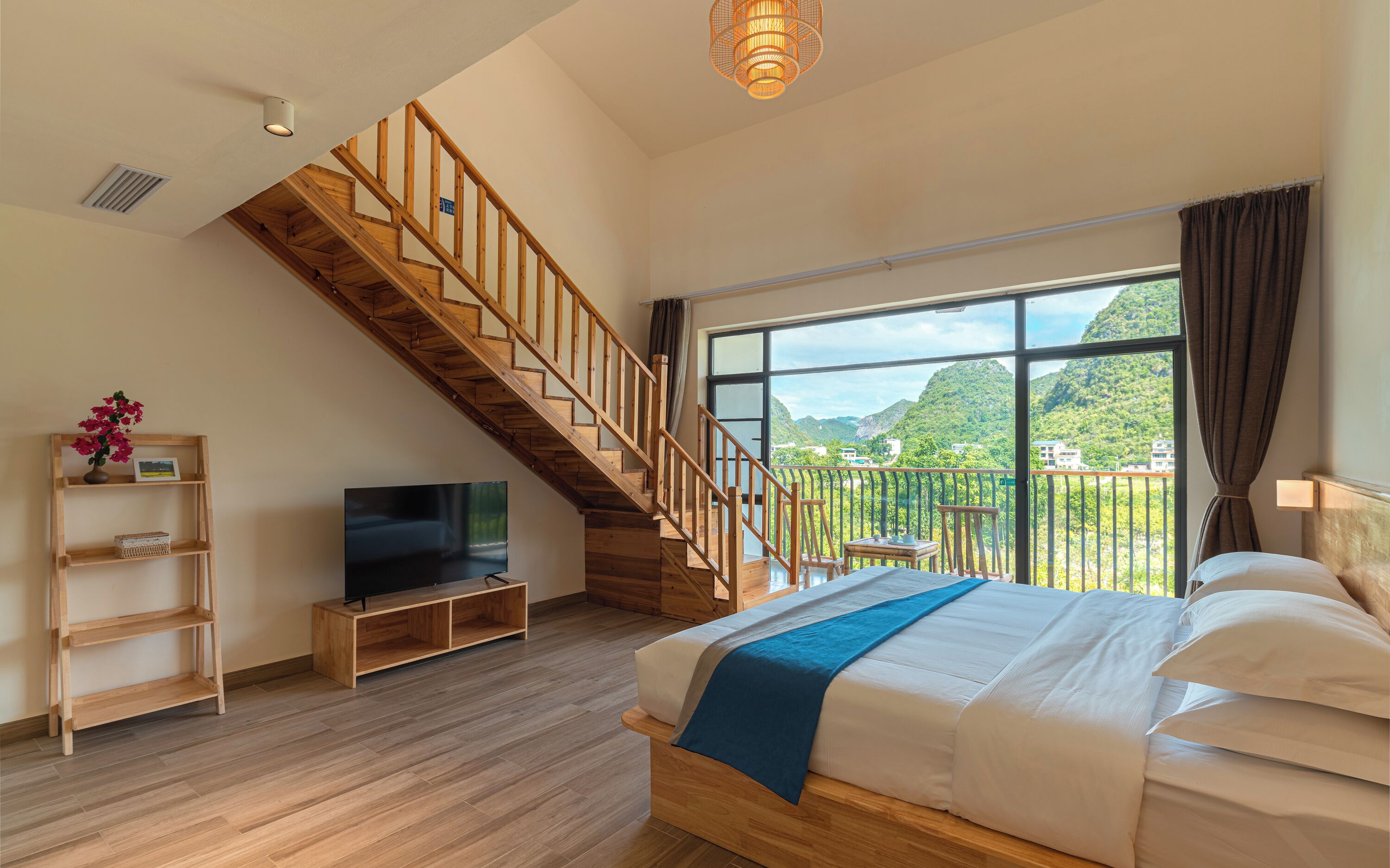 Un dormitorio con una escalera de madera, una cama con ropa de cama blanca, un televisor sobre un soporte de madera y un ventanal con vistas a la vegetación.
