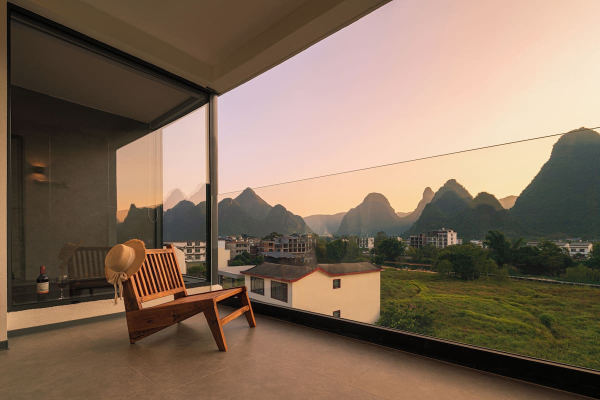 Un balcón con banca de madera y un sombrero, con vistas a un paisaje montañoso con edificios.