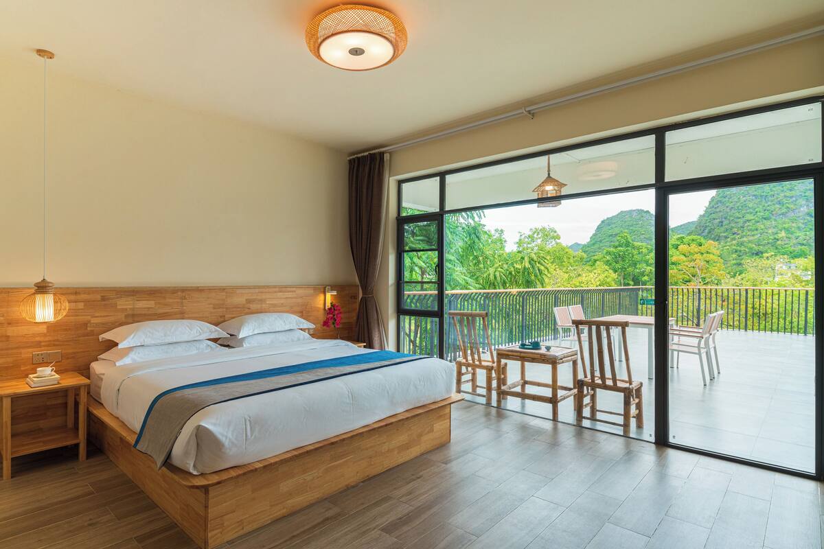 Un dormitorio con una cama grande, mesitas de noche, un balcón con sillas y vistas al verdor.