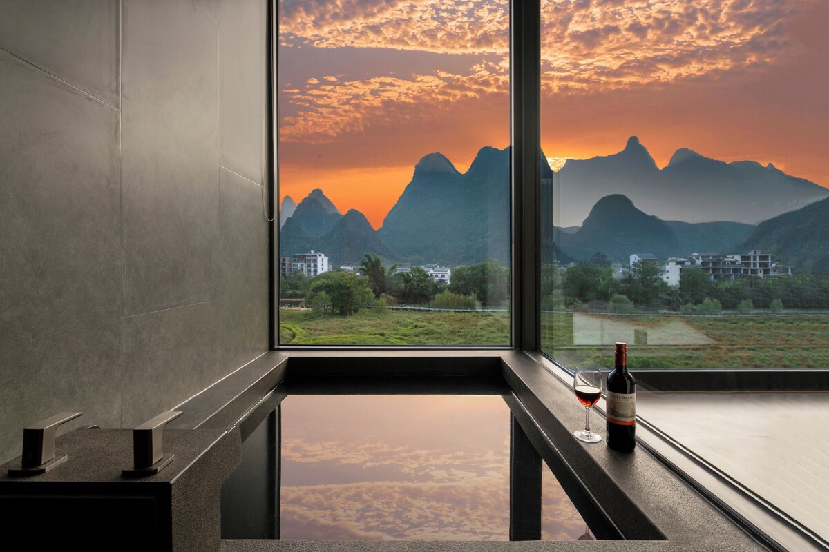 A modern interior with a large window offering a view of mountains and a sunset.