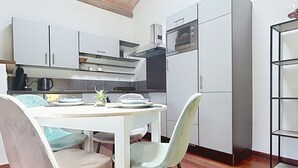 A modern kitchen with white cabinets, a dining table with chairs, and a built-in oven. - Large 40 M2 studio ideal for curists at the Eugénie les Bains thermal baths (Bahus-Soubiran)