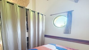A bedroom with a wooden ceiling, a window with curtains, and a bed with a multicolored quilt. - Large 40 M2 studio ideal for curists at the Eugénie les Bains thermal baths (Bahus-Soubiran)