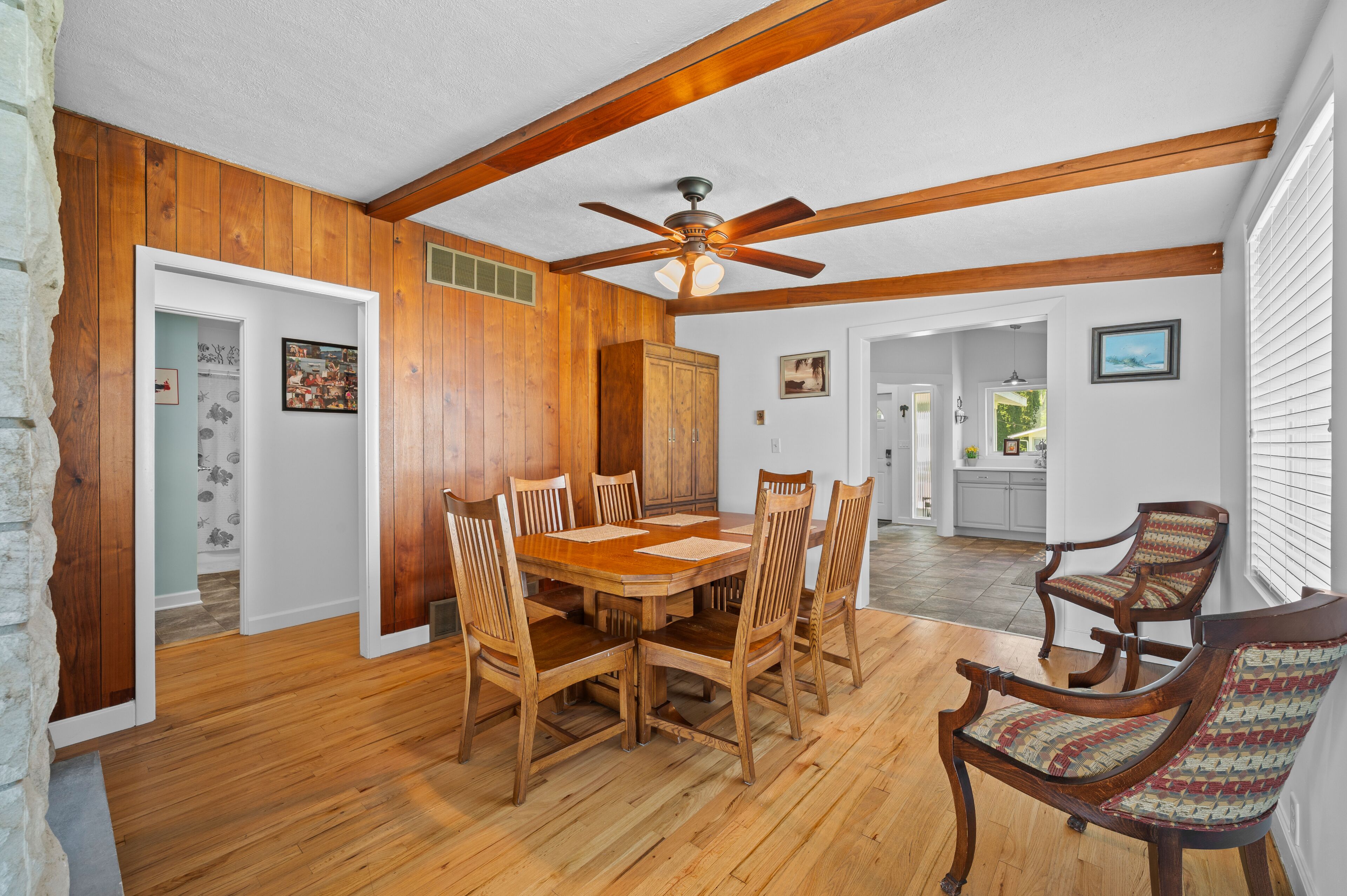 A dining area with a wooden table and chairs, a ceiling fan, and wooden beams.
