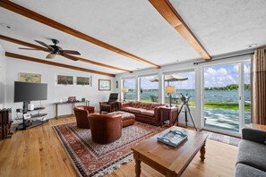 Ein geräumiges Wohnzimmer mit großem Fenster, Deckenventilator, Ledersofa, Couchtisch und Fernseher.