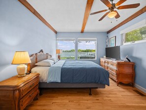 Ein Schlafzimmer mit Bett, Holzkommode, Fernseher und Deckenventilator.