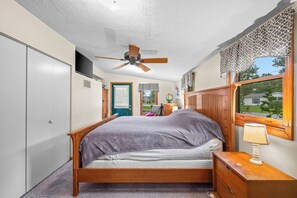 A bedroom with a bed, a nightstand, a lamp, a ceiling fan, a wardrobe, a window with a view, and a door with a window. - Stealth Cottage – Vintage Stay Across from Paw Paw Lake (Coloma)
