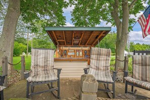 A covered outdoor seating area with striped chairs and a bar counter. - Stealth Cottage – Vintage Stay Across from Paw Paw Lake (Coloma)