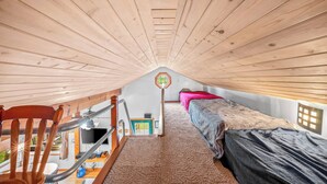 A loft bedroom with a sloped ceiling, a wooden chair, a bed, and a television.