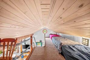 A loft bedroom with a sloped ceiling, a wooden chair, a bed, and a television. - Stealth Cottage – Vintage Stay Across from Paw Paw Lake (Coloma)