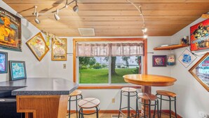 A bar area with a wooden ceiling, a large window with a view of a grassy area, and several framed pictures on the walls.