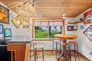 A bar area with a wooden ceiling, a large window with a view of a grassy area, and several framed pictures on the walls. - Stealth Cottage – Vintage Stay Across from Paw Paw Lake (Coloma)