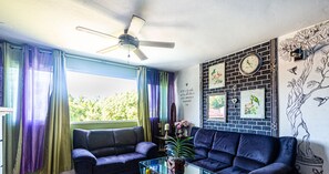 Ein Wohnzimmer mit zwei dunklen Sofas, einem Glastisch und einem Deckenventilator.