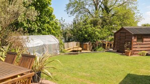 Een achtertuin met een houten tafel, stoelen, een tuinhuis en een houten hutje.