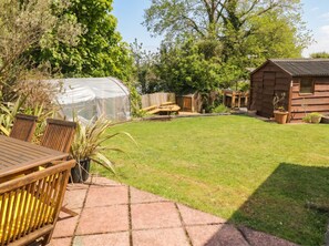 A backyard with a wooden table, chairs, a greenhouse, and a wooden cabin. - 1 Rosemount Garden Villas (Tenby)