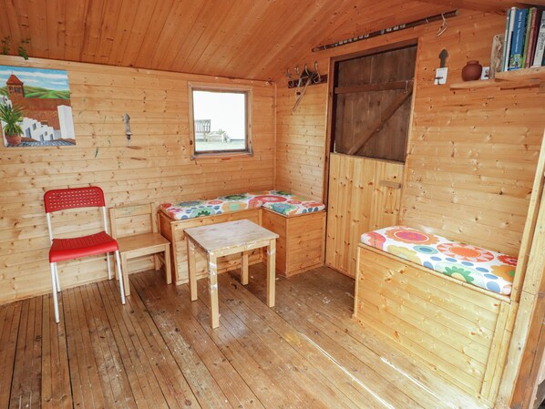 A wooden cabin interior with a bench, a table, a chair, and a window. - 1 Rosemount Garden Villas (Tenby)