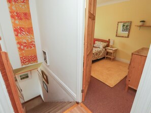 A bedroom with a bed, bedside table, and a small shelf with a plant. - 1 Rosemount Garden Villas (Tenby)