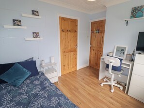 A bedroom with a bed, a desk, a chair, wooden doors, and shelves with pictures. - 1 Rosemount Garden Villas (Tenby)