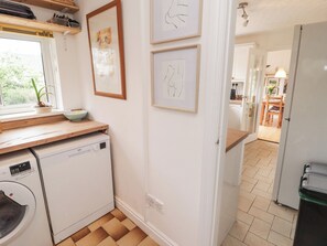 A kitchen with a dishwasher, a window with a plant, and framed artwork on the wall. - 1 Rosemount Garden Villas (Tenby)