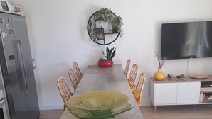 Une cuisine moderne dotée d’un îlot central, d’une table à manger avec des chaises, d’un réfrigérateur, d’un téléviseur et d’un élément décoratif mural.