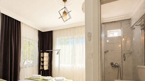 A hotel room with a bed, a bedside table, a shower area, and a window with curtains.