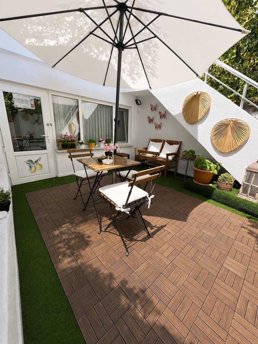 An outdoor patio with a table and chairs, surrounded by a brick floor and green artificial grass.