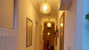 Un pasillo con suelo de baldosas, obras de arte enmarcadas en las paredes y un aplique de techo.
