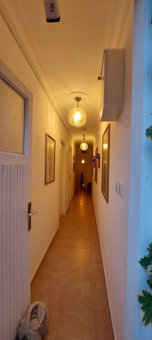 A hallway with a tiled floor, framed artwork on the walls, and a ceiling light fixture. - Hil Ada Otel (Bozcaada)