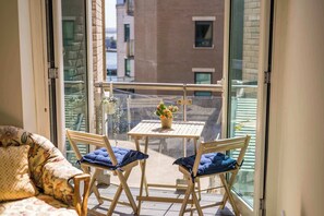 Ein Balkon mit Tisch, Stühlen, einer Couch und Blick auf Gebäude.