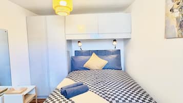 Un dormitorio con una colcha a cuadros, un cabecero azul, una lámpara colgante amarilla y un cuadro en la pared.