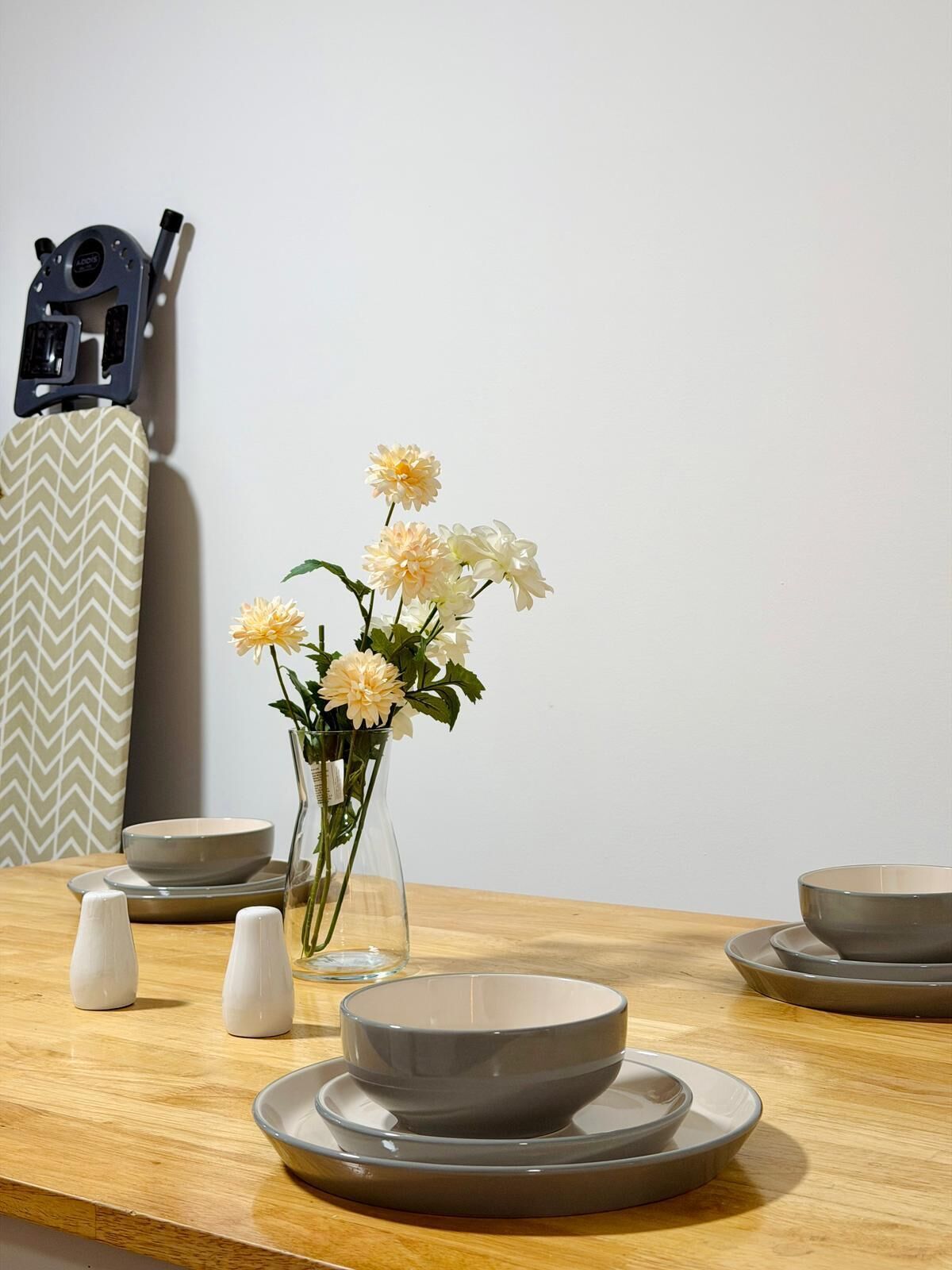 A dining table with a vase of flowers, bowls, and salt shakers.