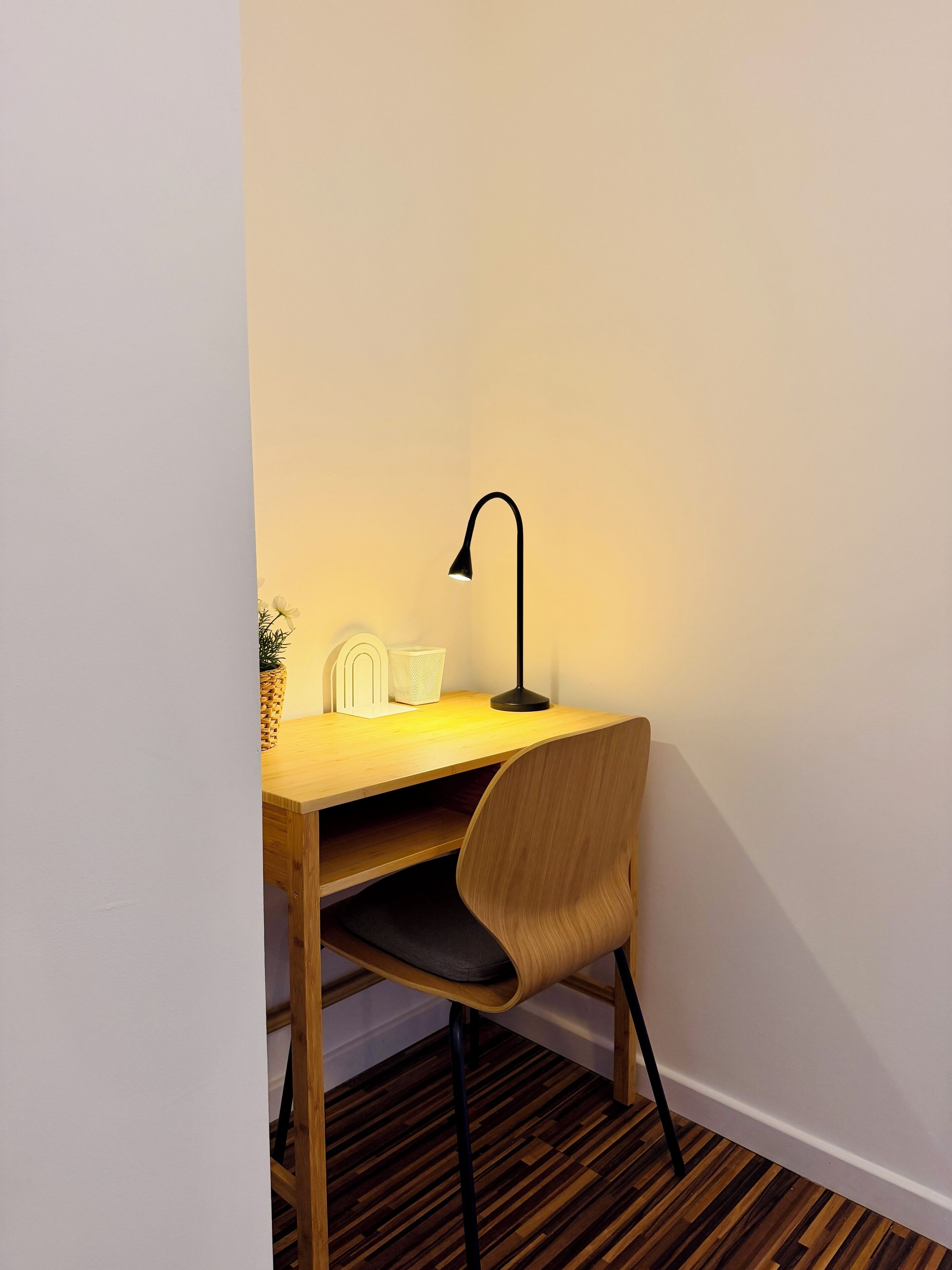 A corner desk with a chair, a desk lamp, and a small plant.