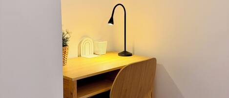 Mesa de canto com cadeira, luminária de mesa e uma pequena planta.