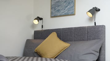 A bedroom with a grey headboard, a checkered blanket, two bedside lamps, and a wall clock.
