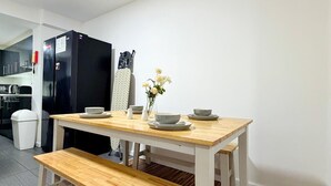 Une cuisine moderne avec un réfrigérateur noir, une table à manger en bois avec des bancs, et un mur blanc.