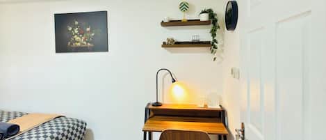 A compact room with a bed, a desk with a lamp, a wooden floor, and a door.