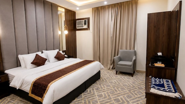 A modern hotel room with a large bed, a seating area, a TV, and a wardrobe.