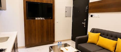 A modern living room with a sofa, coffee table, TV, and a kitchen area.