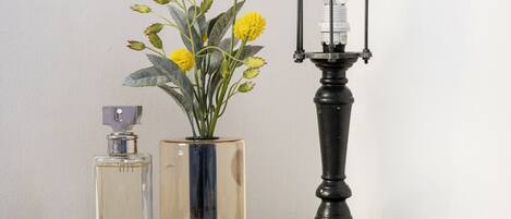 A wooden table with a lamp, a vase with yellow flowers, a perfume bottle, and a folded white cloth.