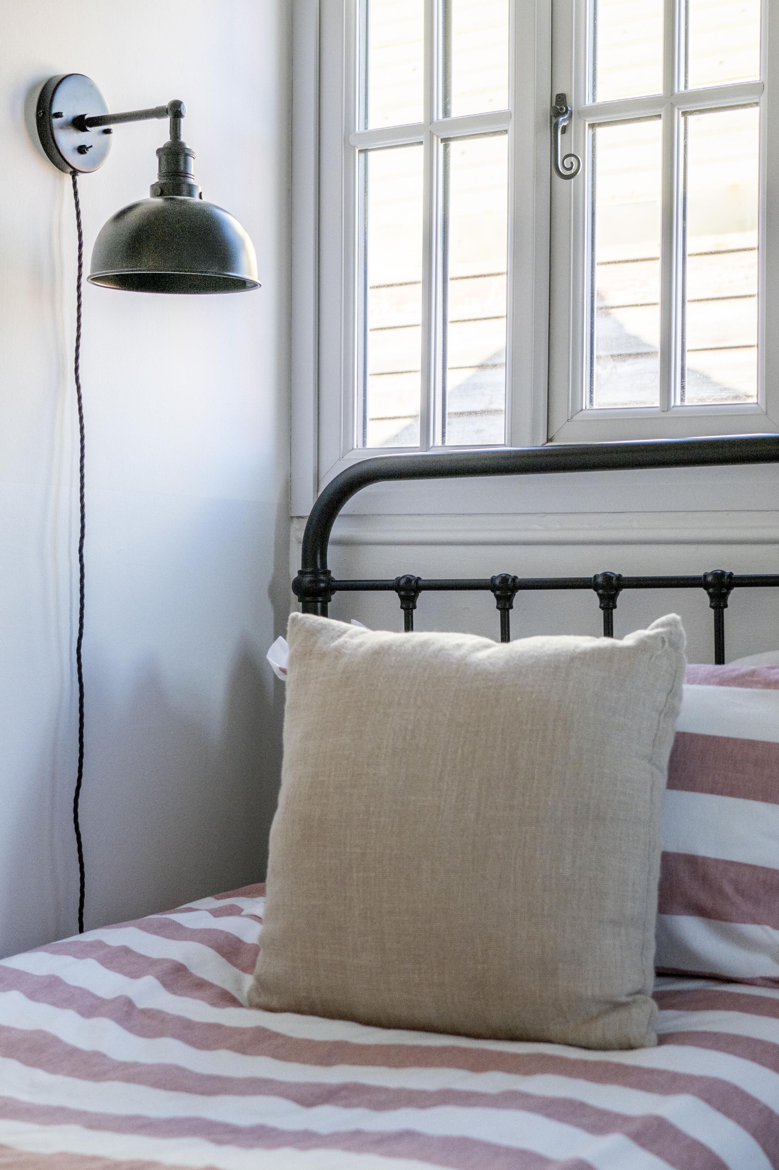 A bed with a striped bedspread, a plain pillow, and a wall-mounted lamp.