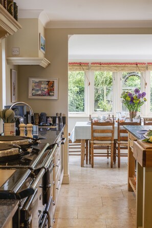 A kitchen with a stove, sink, and dining table with chairs. There is a window with a view of greenery outside.