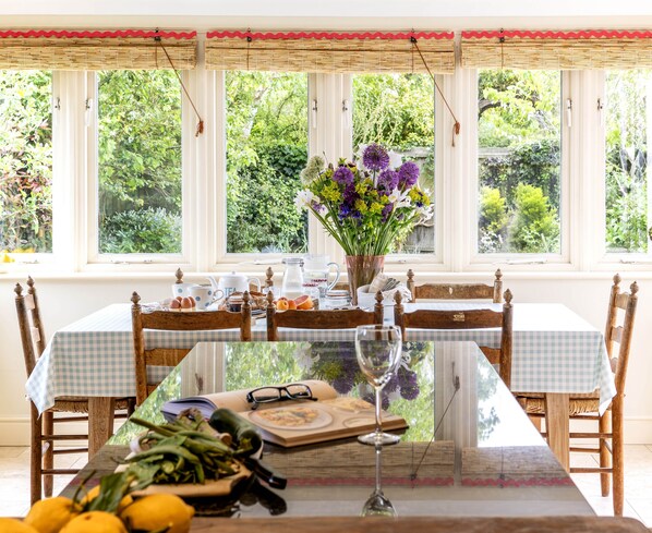 A dining table with chairs, a glass top, and a vase with flowers.