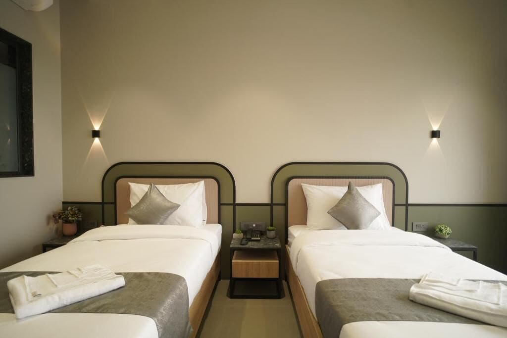 Une chambre d’hôtel avec deux lits simples, chacun équipé d’un oreiller, d’une table de chevet avec un téléphone et une petite plante, ainsi que d’un luminaire fixé au mur.